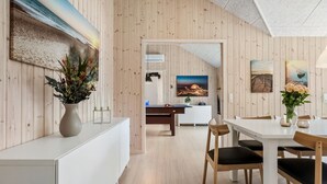 Ein modernes Interieur mit Holzwandverkleidung, einem Essbereich mit weißem Tisch und Stühlen sowie Kunstwerken an den Wänden.