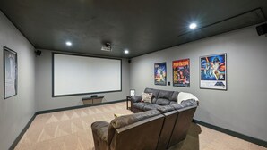 Un salón de cine en casa con una pantalla grande, un sillón de cuero reclinable y carteles en la pared.