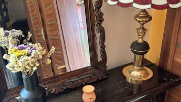 A wooden dresser with a mirror, a vase with dried flowers, and a table lamp.