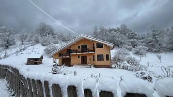 Een huis met twee verdiepingen, met een balkon, omringd door met sneeuw bedekte bomen en een houten hek.