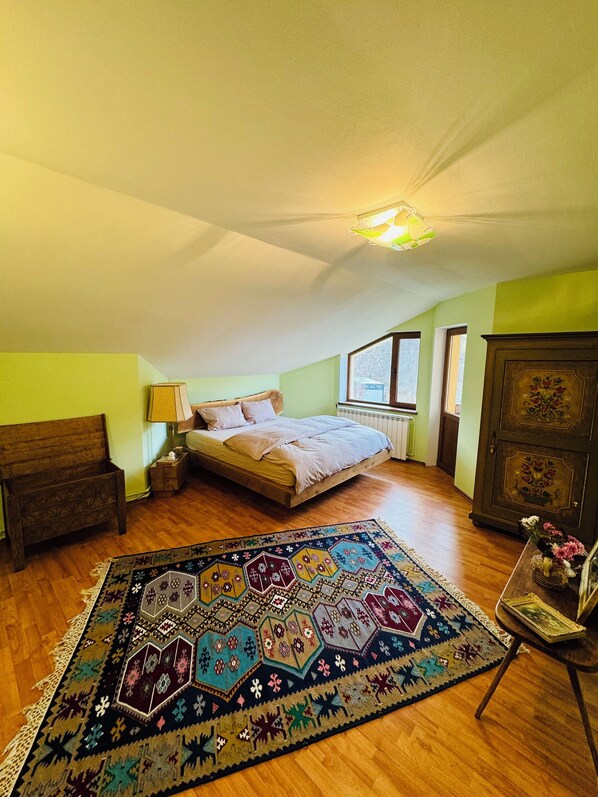 A bedroom with a wooden bed, a colorful rug, a nightstand, a dresser, and a window. - Rai Villa (Banita)