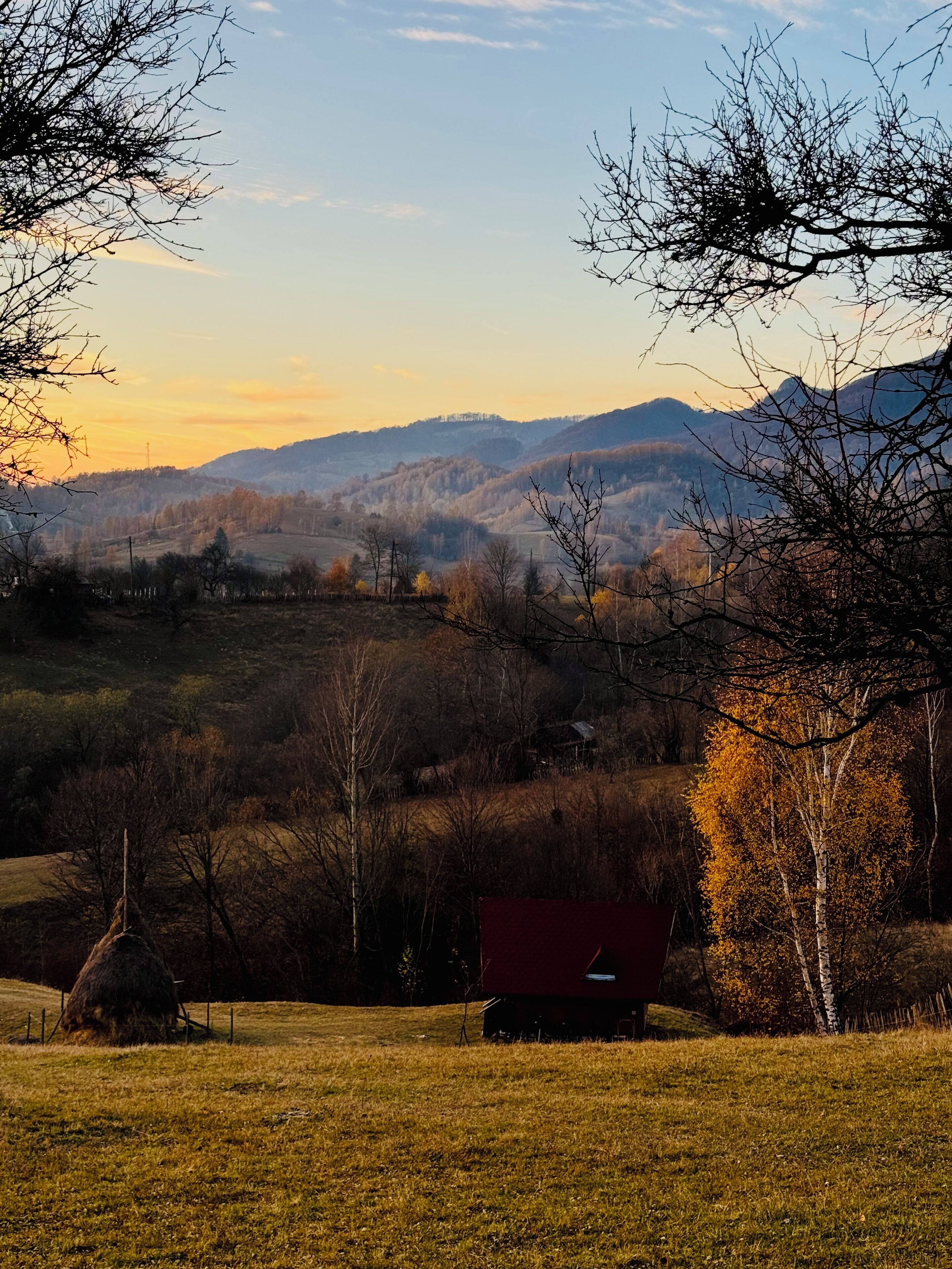 A rural landscape with a red cabin in the foreground, surrounded by trees and hills in the background.