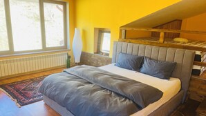 A bedroom with a large bed, a wooden headboard, a radiator, a window, and a view of trees. - Rai Villa (Banita)