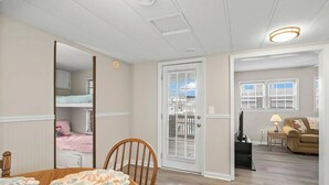A room with a wooden dining table, a chair, a bunk bed with pink bedding, a white door, and a view of the outside through a window with blinds. - 1309 Ocean Lakes Pet Friendly Golf Cart⛱️🏝️🩱🌊👙☀️🐚 (Myrtle Beach)