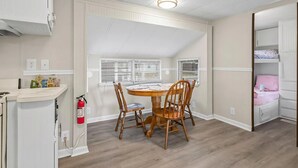 A compact kitchen with a dining table and chairs, a built-in bench, and a window with blinds. - 1309 Ocean Lakes Pet Friendly Golf Cart⛱️🏝️🩱🌊👙☀️🐚 (Myrtle Beach)