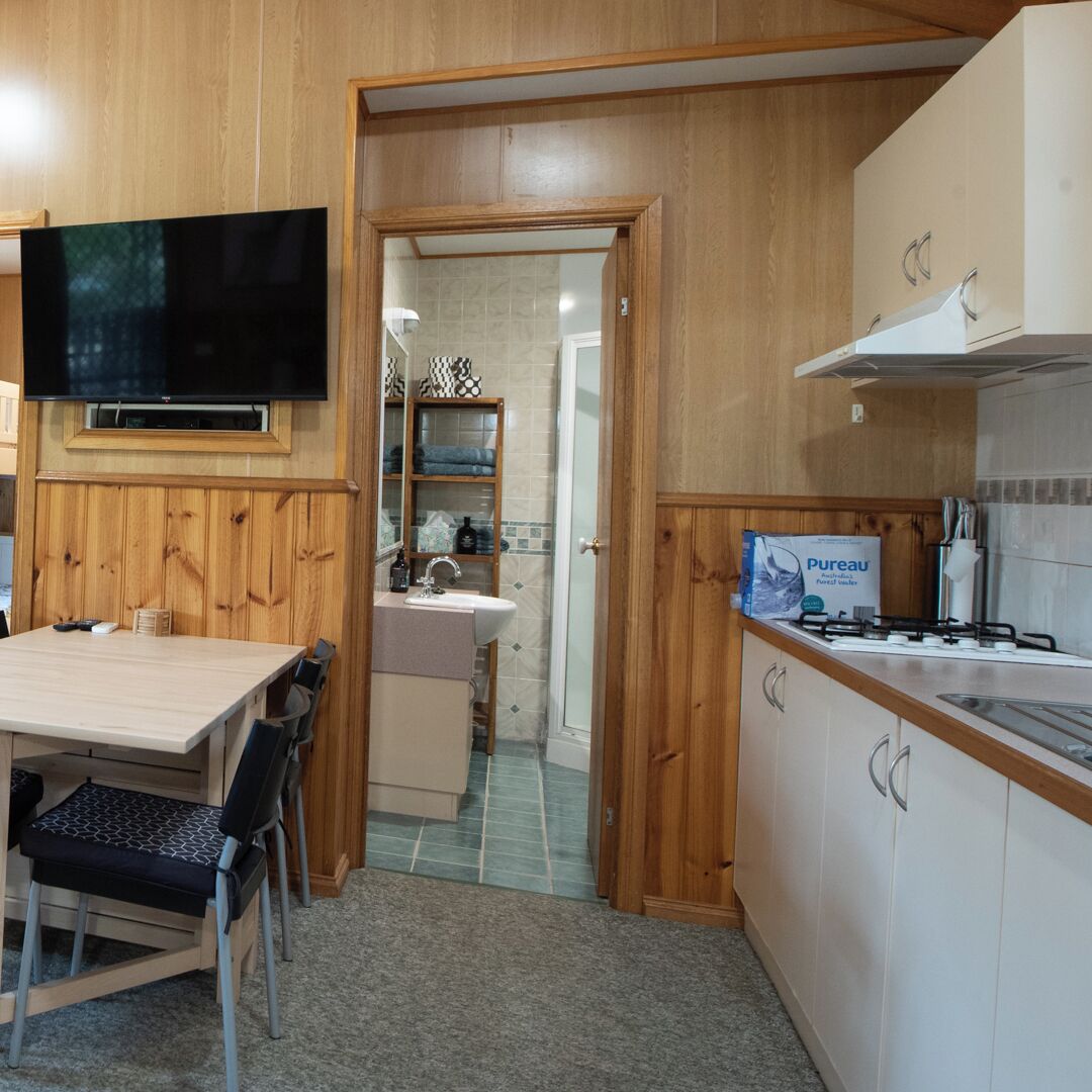 A compact kitchen with wooden cabinetry, a built-in stove, and a television mounted above the counter.