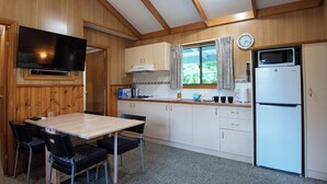 Een compacte keuken met houten wanden, een eettafel met stoelen, een magnetron en een koelkast.