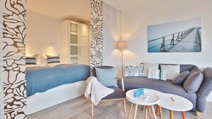 A modern hotel room with a bed, a sofa, a small table, and a painting of a bridge.