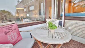 A cozy outdoor seating area with a round wooden table, a cushioned bench, and a potted plant.