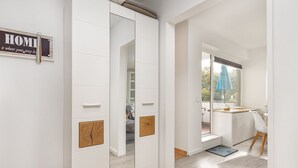 A modern, minimalist hallway with white walls and wooden accents, leading to a balcony with a view.