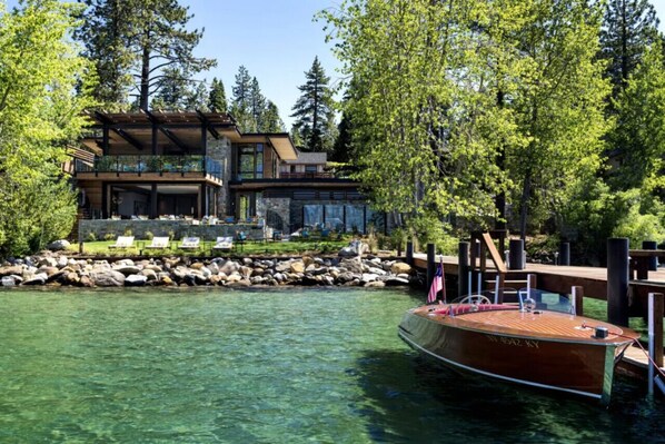 A waterfront property with a dock, a boat, and a building with a deck and lounge chairs.