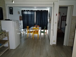 A compact kitchen with a refrigerator, a dining table with chairs, and a window with curtains. - Studio 4 persons  (Leucate)
