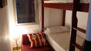 Un lit superposé avec une structure rouge, une petite table de chevet avec une lampe et une fenêtre avec des rideaux.
