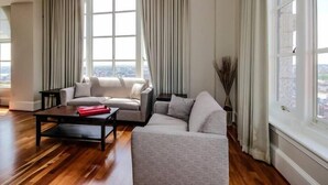A spacious living room with a large arched window, a grey sofa, a coffee table, and a view of the city. - Baltimore executive Furnished rentals (Baltimore)