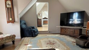 A living room with a large flat-screen TV, a blue armchair, a patterned rug, and a wooden cabinet. - Come enjoy the Victorian charm of this beautiful home. (La Junta)