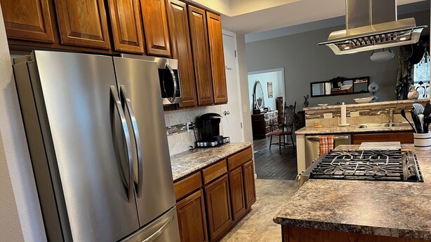 A modern kitchen with wooden cabinets, stainless steel appliances, a granite countertop, and a central island with a stove. - Come enjoy the Victorian charm of this beautiful home. (La Junta)