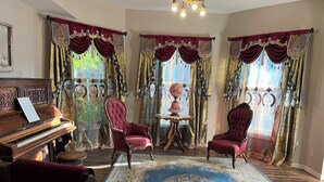 A room with a grand piano, two red upholstered chairs, a small table with a globe, and ornate curtains. - Come enjoy the Victorian charm of this beautiful home. (La Junta)