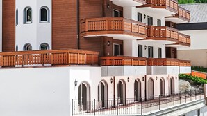 A multi-story hotel with wooden balconies and arched windows, set against a mountainous backdrop.