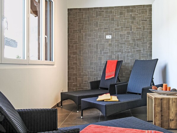 A room with a tiled floor, a window, and a wall with a geometric pattern. There are two chairs and a small wooden table with candles.