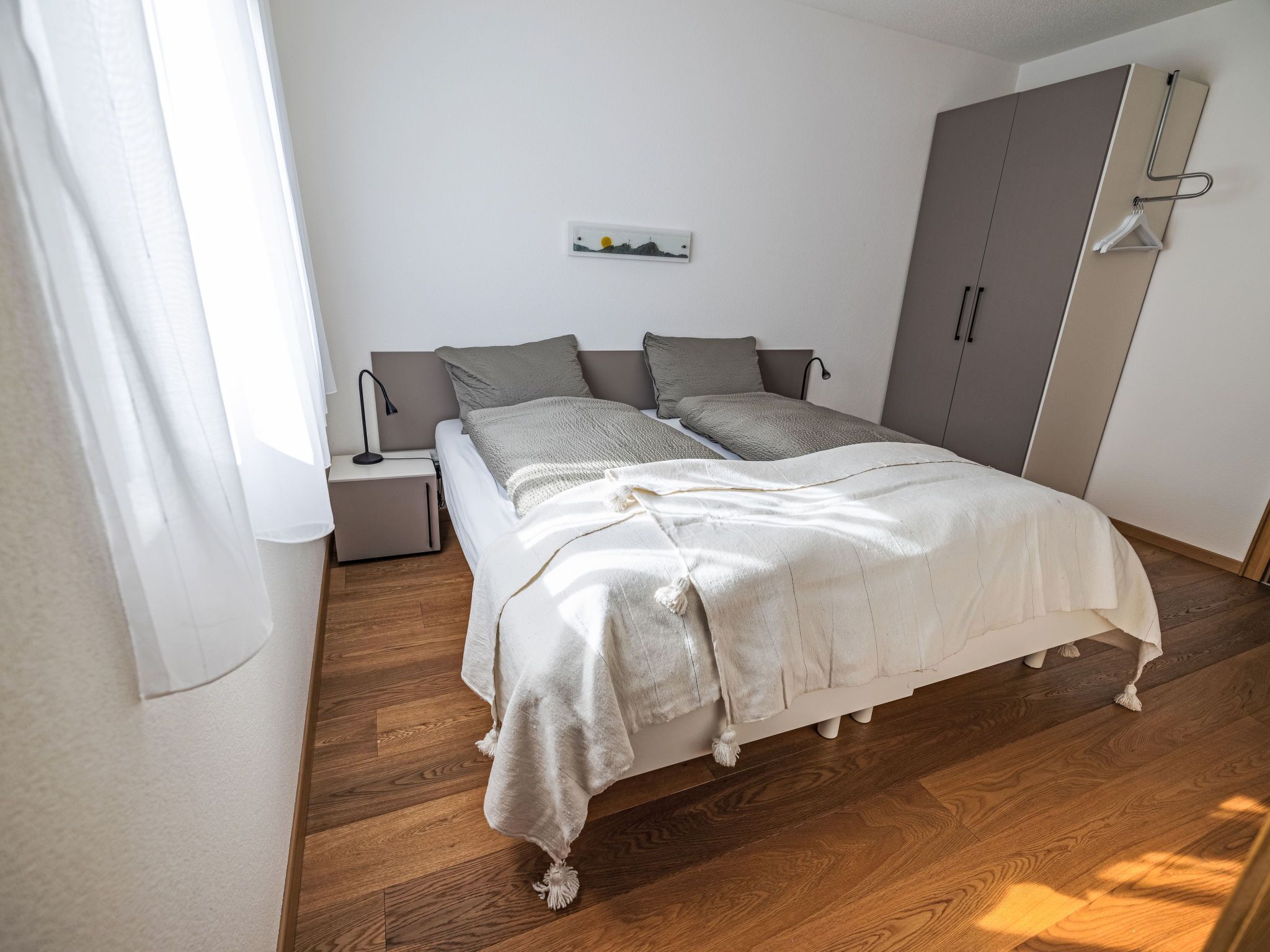 A bedroom with a bed, nightstand, wardrobe, and a wall-mounted picture.