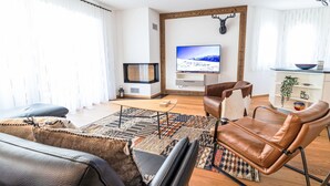 A modern living room with a flat-screen TV, leather sofas, a patterned rug, and a wooden floor.