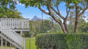 A white wooden staircase leading to a deck, surrounded by well-maintained hedges and trees.