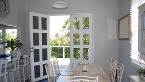A dining area with a table set for four, white chairs, a potted plant, and a view through a glass door to the outdoors.