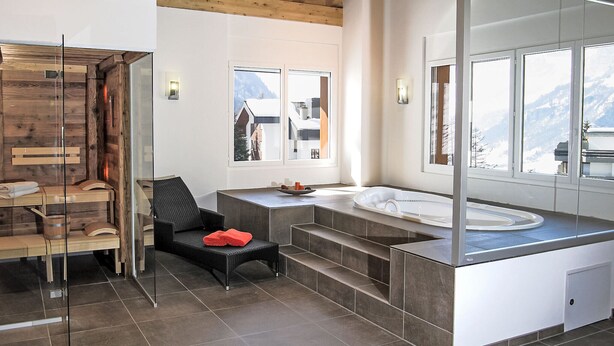 A modern bathroom with a wooden ceiling, a large mirror, a bathtub, and a chair.