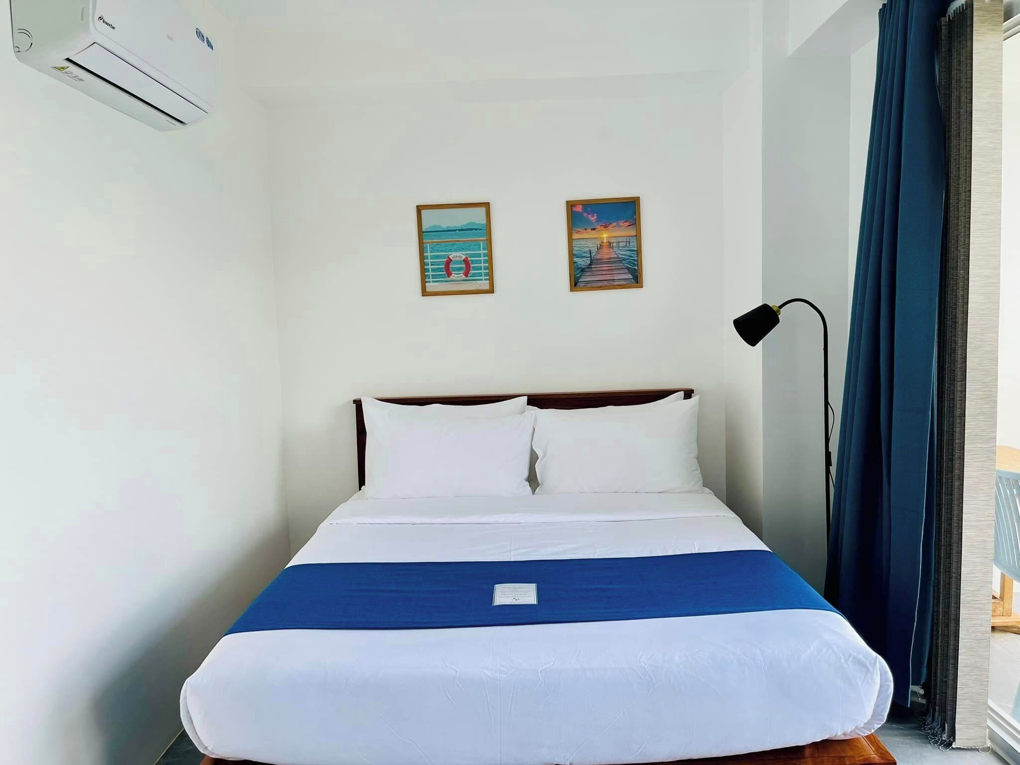 A hotel room with a bed, a nightstand, a lamp, and two paintings on the wall.