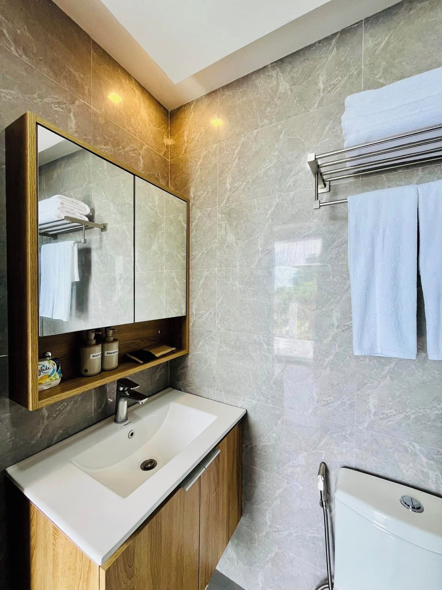 Un baño moderno con pared de mármol, un espejo grande, un mueble de tocador de madera y un perchero para toallas.