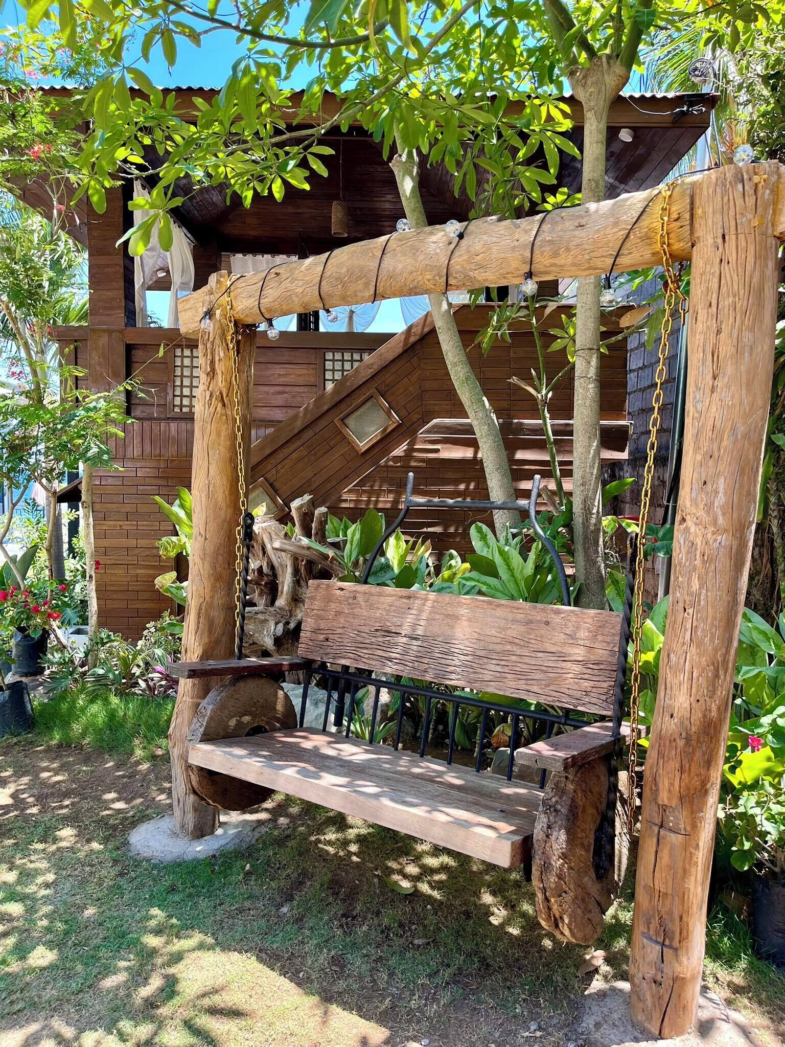 A rustic wooden bench with a slatted seat and backrest, supported by a wooden frame with chains.
