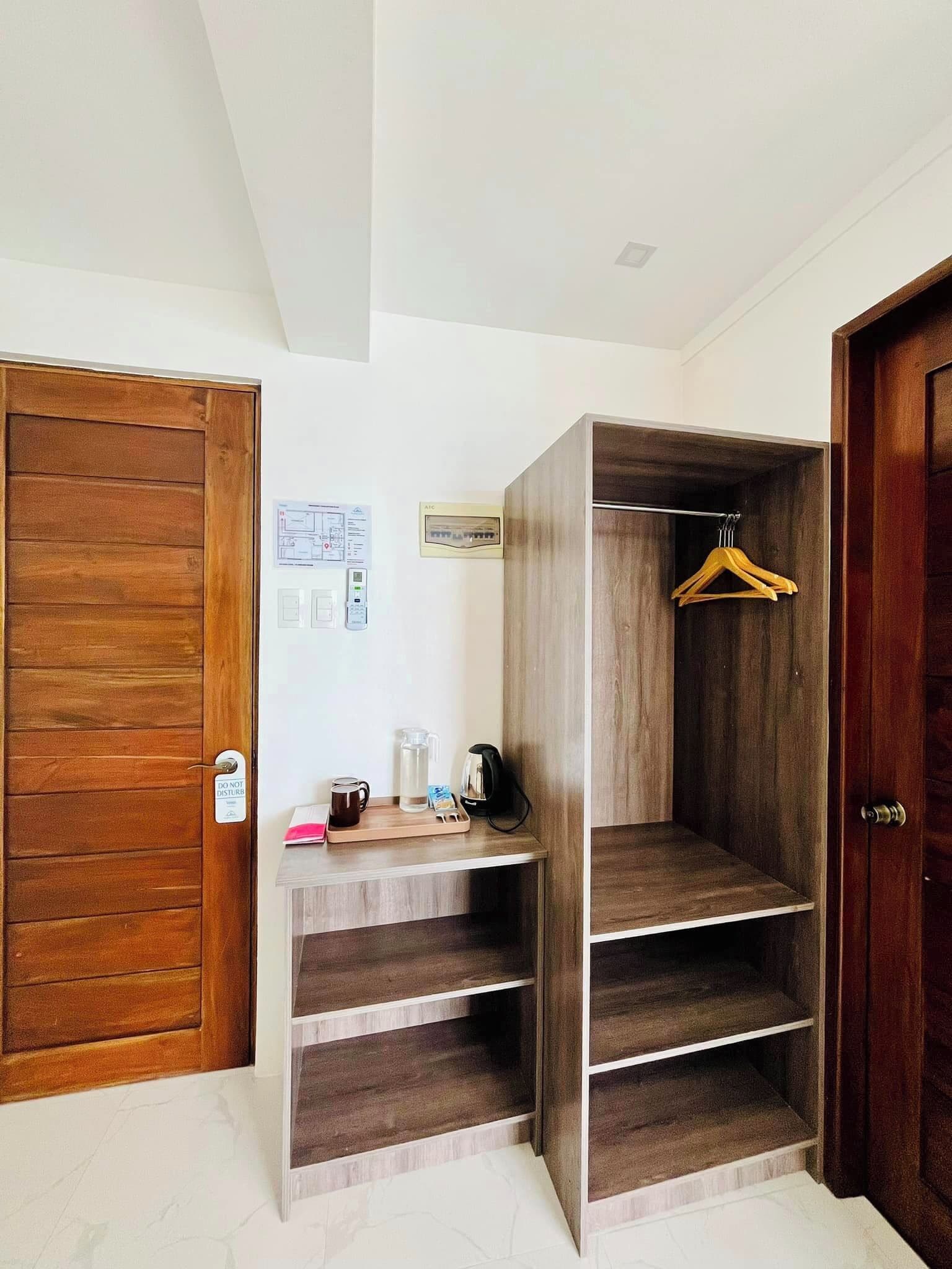 A room with a wooden wardrobe, a wooden wardrobe with shelves, a coat rack, and a wall-mounted electrical panel.