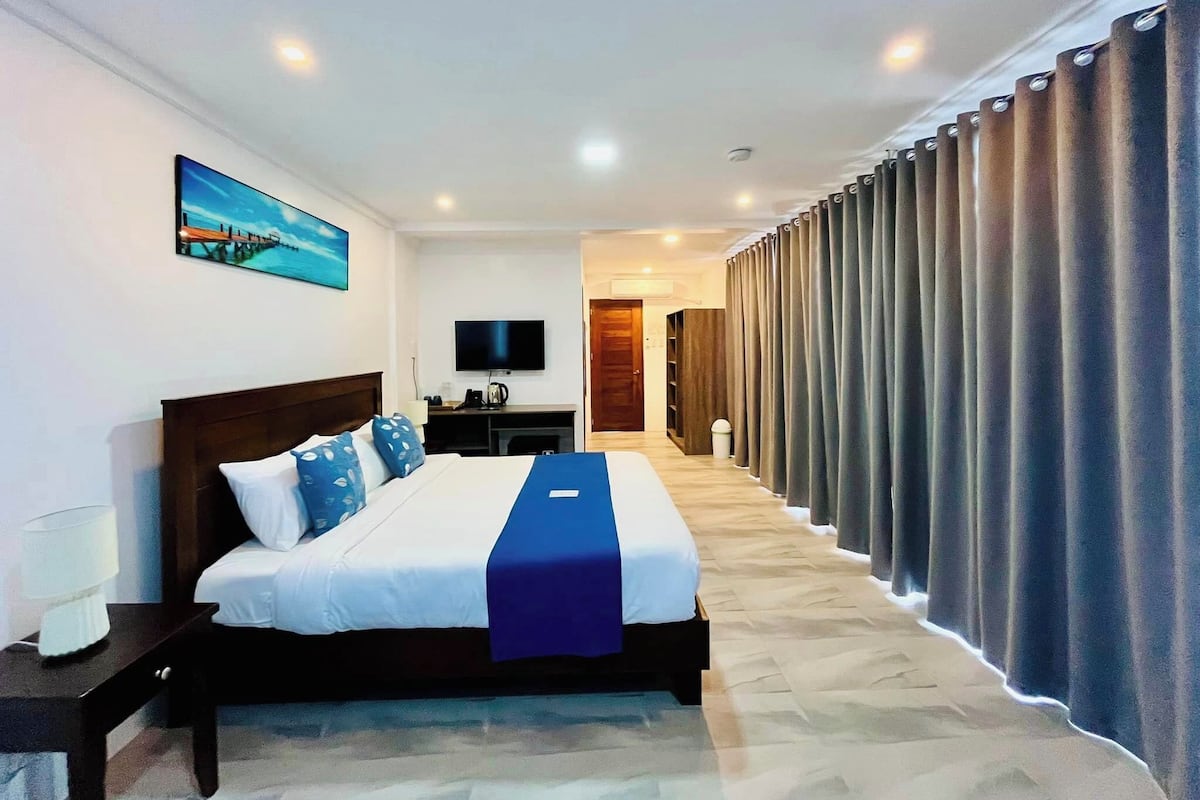 A hotel room with a large bed, a TV, a desk, and a view of the corridor.