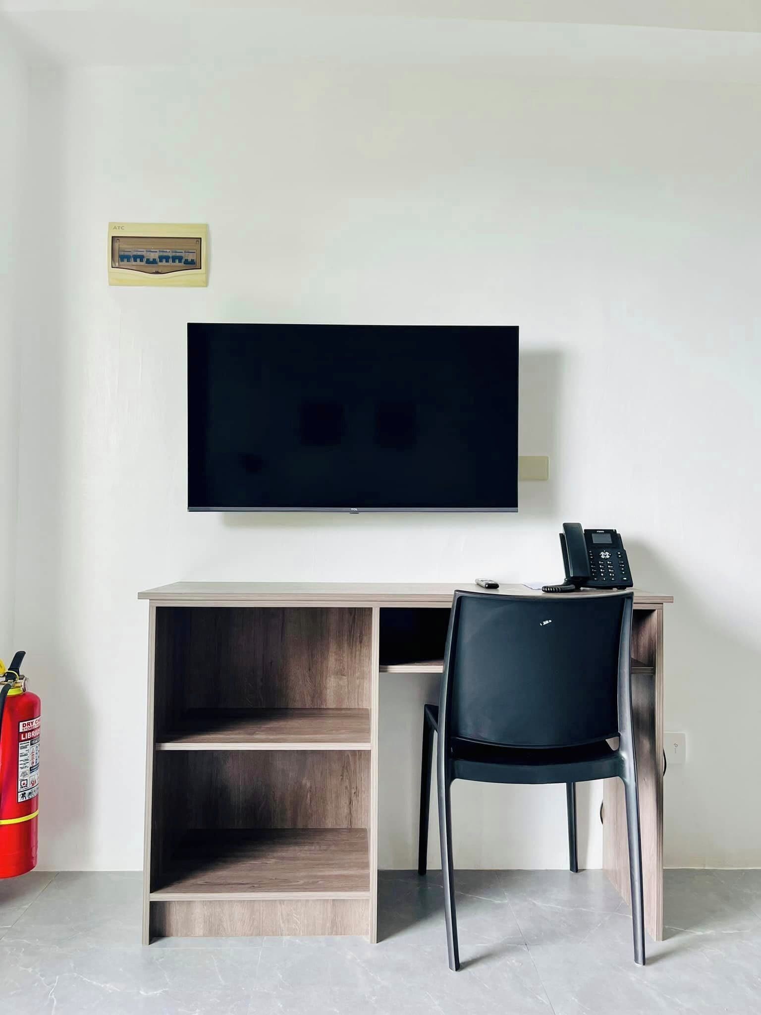 A modern office space with a flat-screen TV mounted on the wall, a desk with a chair, and a fire extinguisher on the floor.