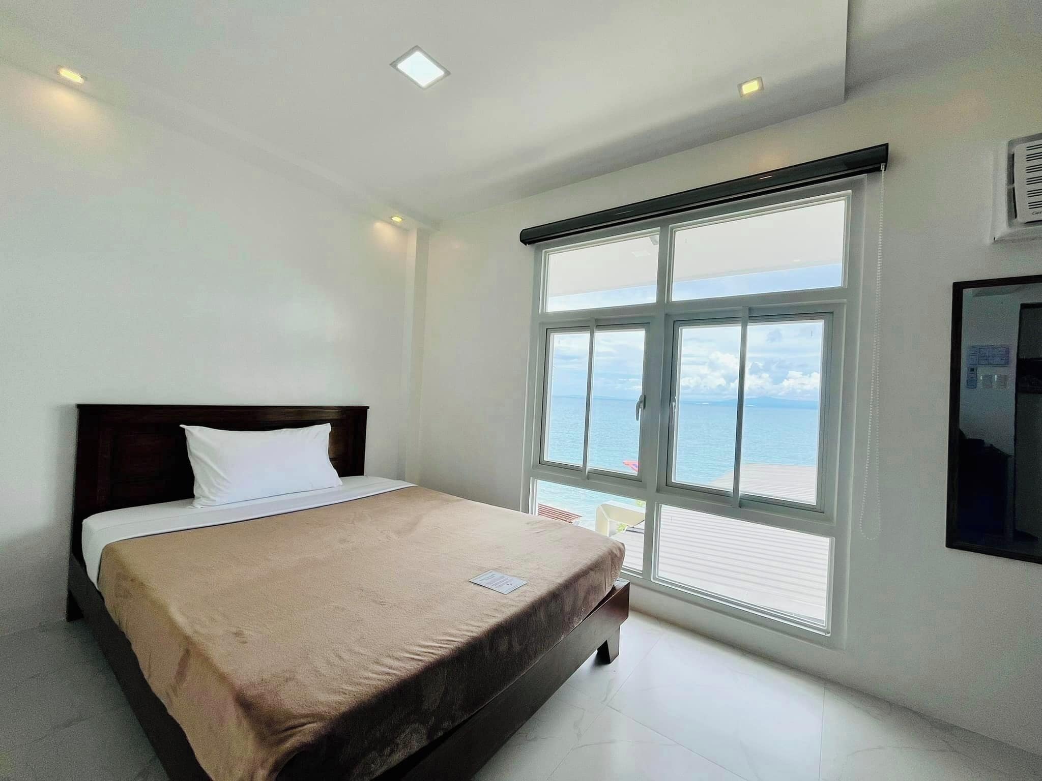 Ein Hotelzimmer mit Bett, großem Fenster und Meerblick sowie einem Wand-Fernseher.