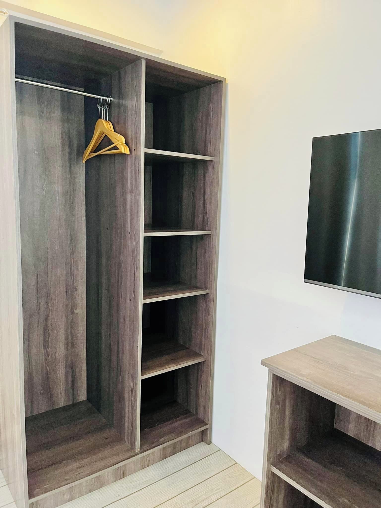 Ein begehbarer Kleiderschrank mit mehreren Regalen und einer Kleiderstange, eine Holzbank und ein Flachbildfernseher an der Wand.