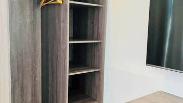 Ein begehbarer Kleiderschrank mit mehreren Regalen und einer Kleiderstange, eine Holzbank und ein Flachbildfernseher an der Wand.