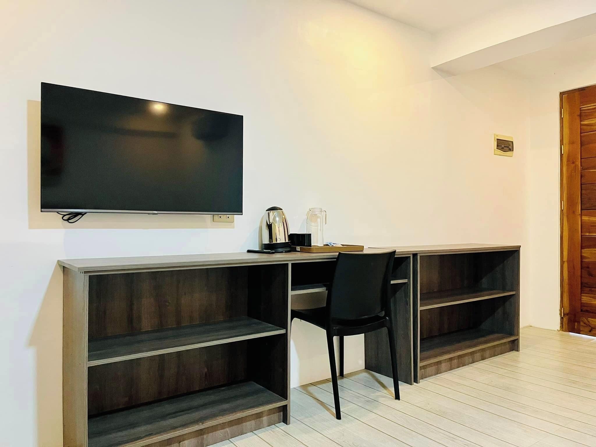 A modern room with a flat-screen TV mounted on the wall, a desk with a chair, and built-in shelving.