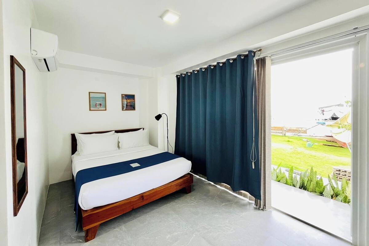A bedroom with a bed, a ceiling light, a window with curtains, and a view of the outdoors.