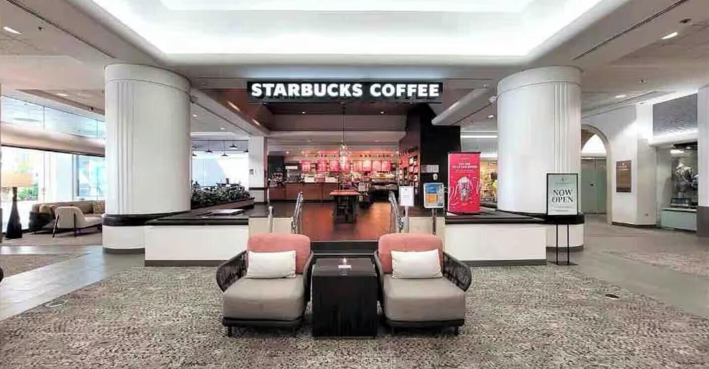 Une enseigne Starbucks devant l’entrée d’un bâtiment moderne, avec des espaces aménagés pour s’asseoir et un intérieur visible.