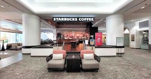 Une enseigne Starbucks devant l’entrée d’un bâtiment moderne, avec des espaces aménagés pour s’asseoir et un intérieur visible.