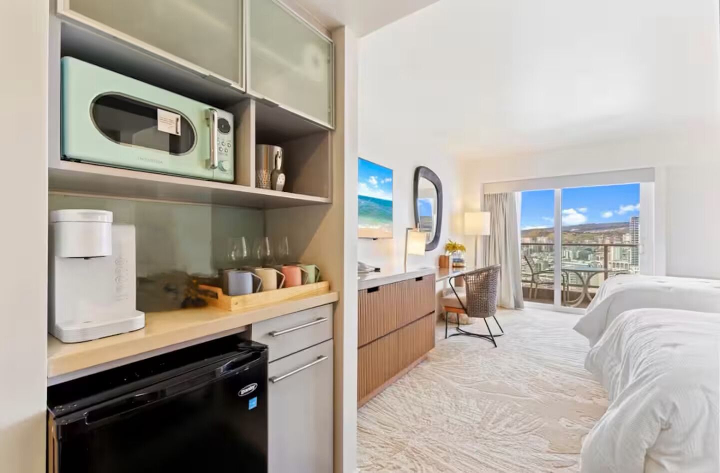 Une chambre d’hôtel équipée d’une kitchenette, d’un lit, d’un bureau et offrant une vue sur la ville.