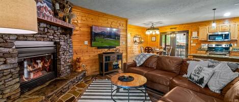 A cozy living room with a stone fireplace, leather sofa, and a television mounted on the wall.