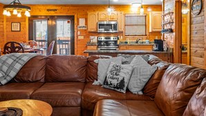 A cozy cabin interior with a leather sofa, wooden cabinets, a kitchen area, and a dining table. - Oasis Escape- Hot Tub, Waterfalls & Cozy Nights (Pigeon Forge)