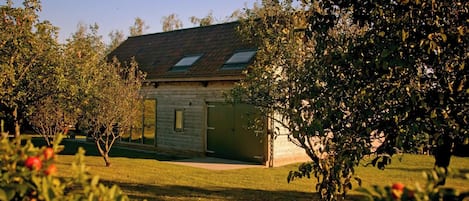 A wooden house with a sloped roof, a visible garage door, and a lawn with trees and shrubs.
