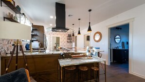 A modern kitchen with a marble island, bar stools, pendant lighting, and a built-in oven. - Kendall Whittier TU, Downtown (Tulsa)