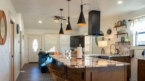 A modern kitchen with a large island, pendant lights, and a dining area with bar stools. - Kendall Whittier TU, Downtown (Tulsa)