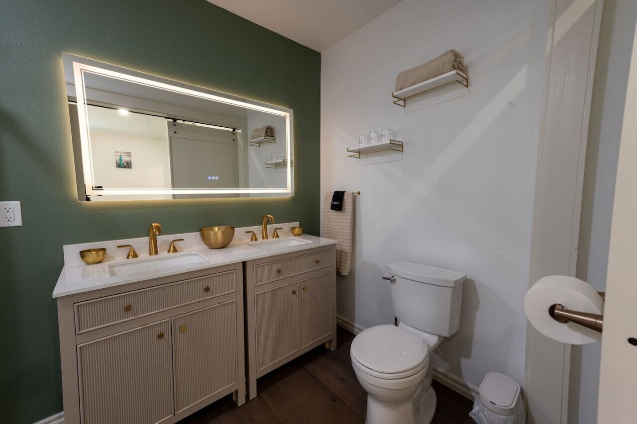 Un bany amb doble lavabo, vàter i un gran mirall amb il·luminació sota els armaris.