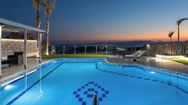 Ein Schwimmbecken mit freiem Blick auf den Sonnenuntergang, Liegestühle und Palmen.