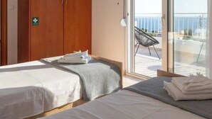 Ein Hotelzimmer mit zwei Betten, einem Holzschrank, einem Erste-Hilfe-Schild und einem Balkon mit einem Stuhl.
